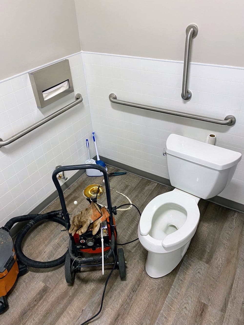 Cleaning equipment and tools near a toilet in a restroom with grab bars.