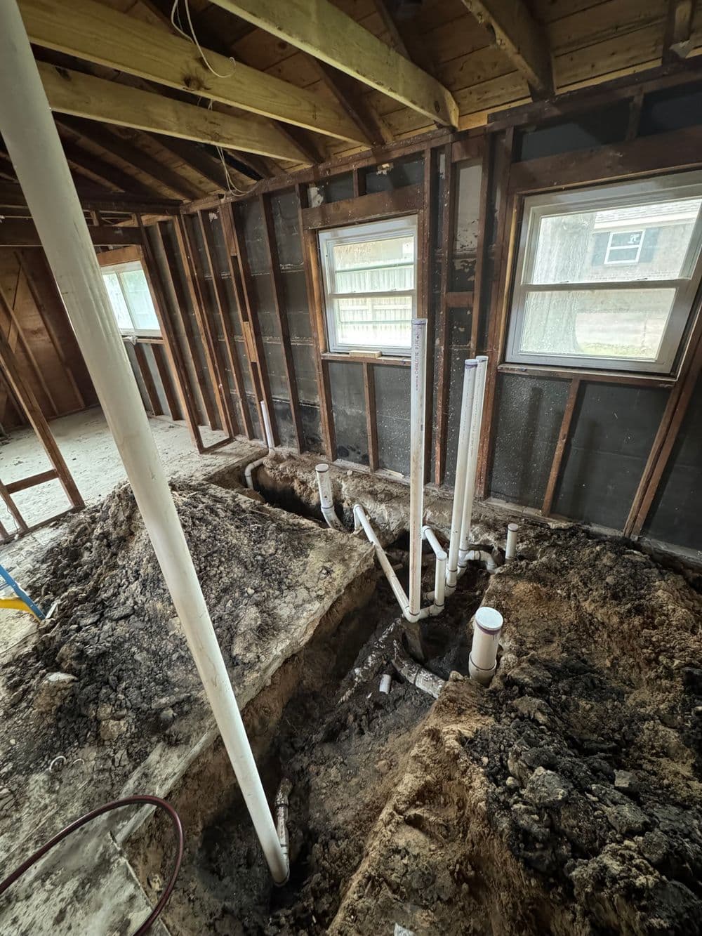 Indoor construction site showing exposed plumbing and piping in a partially finished room.