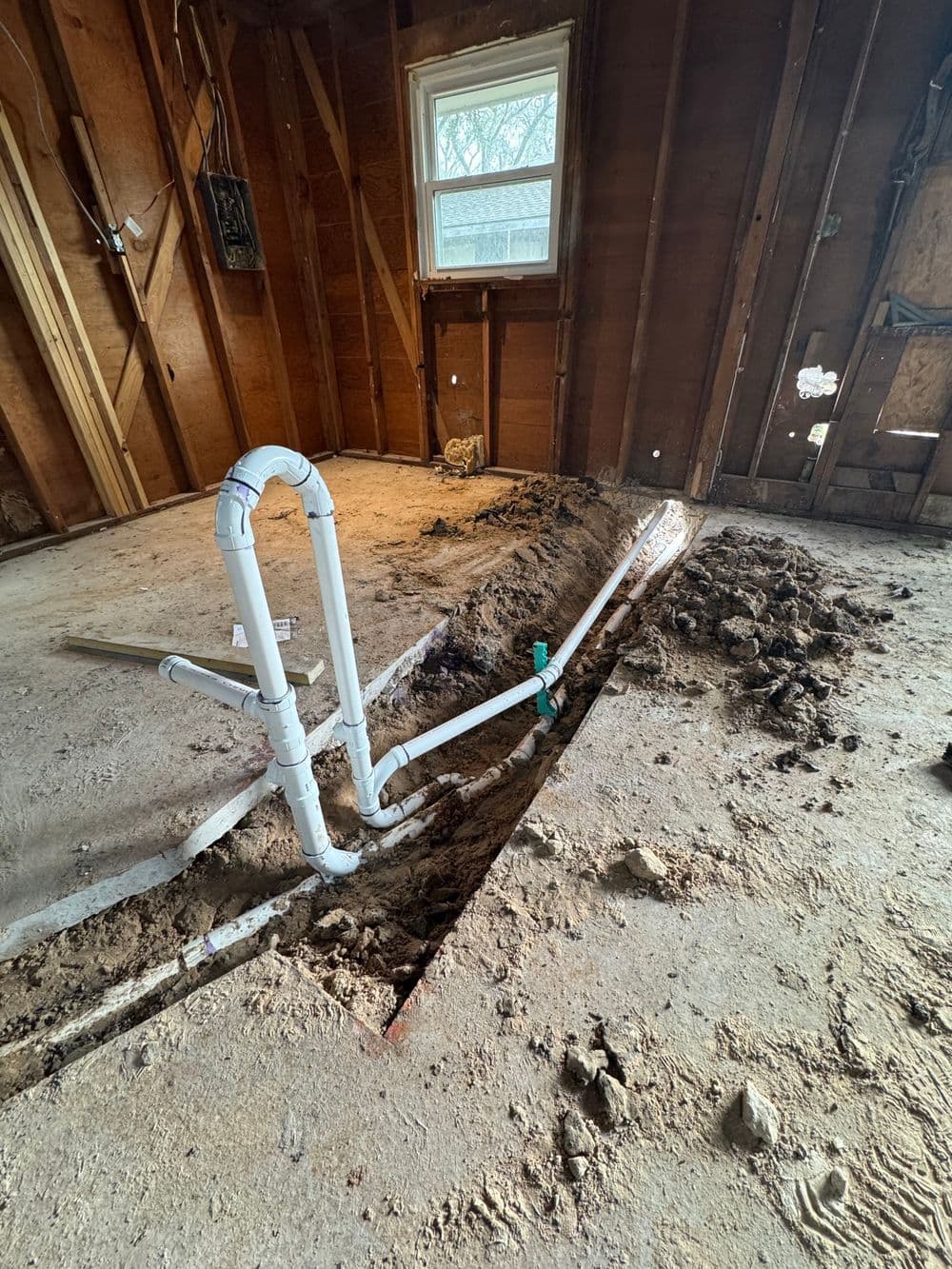 exposed plumbing pipes in a gutted room with dirt and floor excavation visible