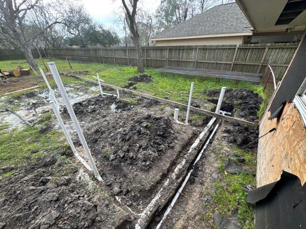 Excavated backyard plot with white PVC pipes and muddy soil for construction project.