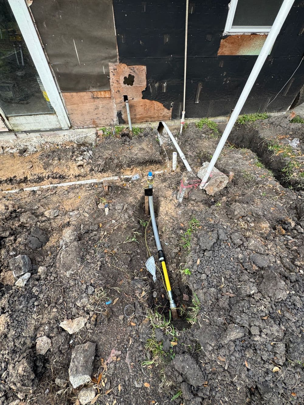 Excavated area showing plumbing pipes and foundation work for home renovation project.