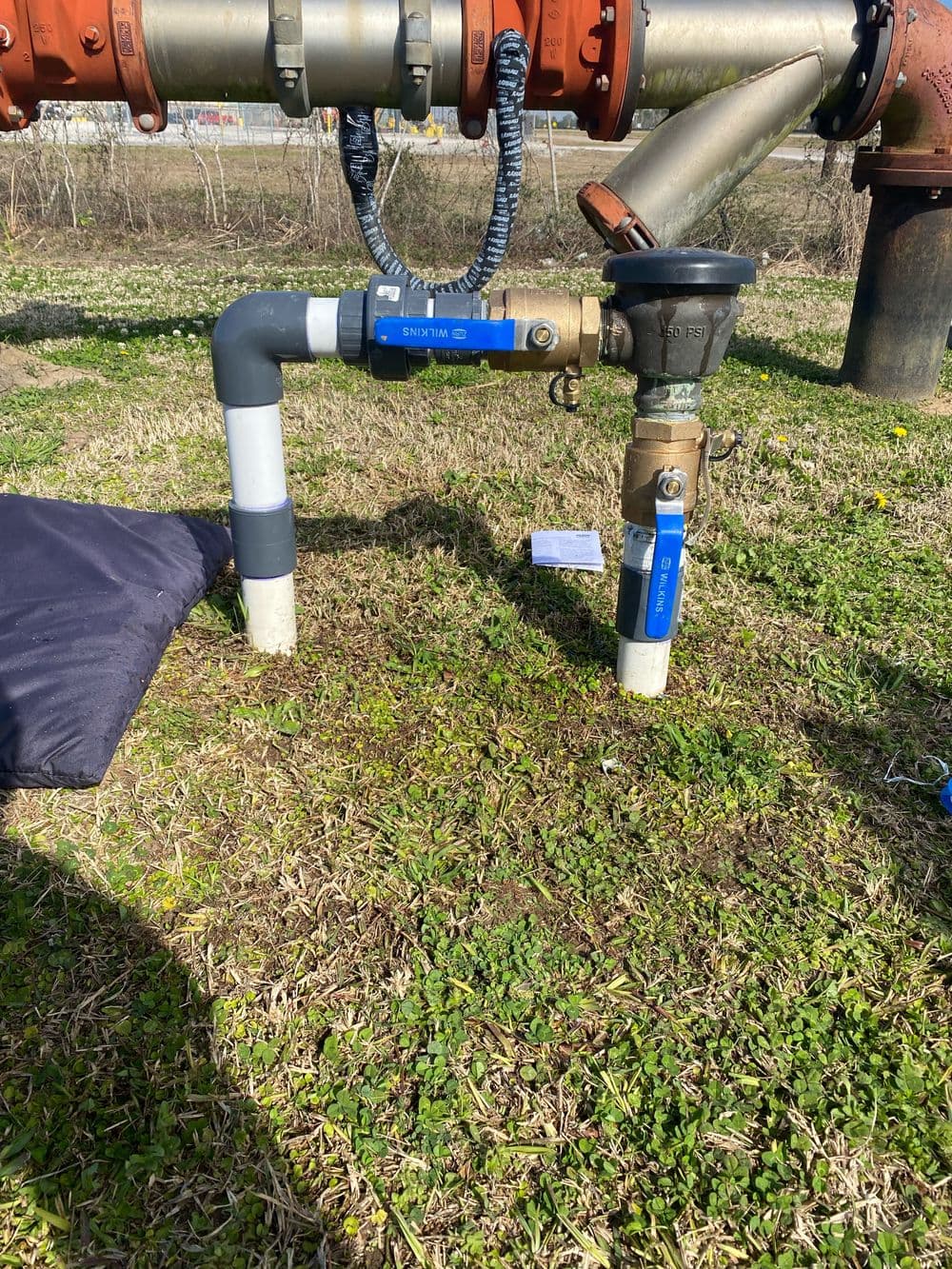 Irrigation system valve with blue fittings on grassy ground near a pipeline.