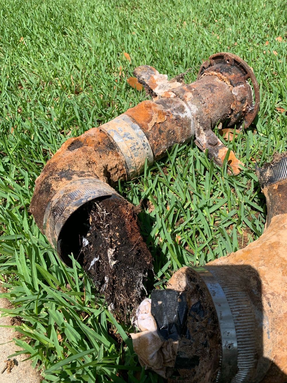 Rusty broken pipe surrounded by green grass, showing signs of deterioration and wear.