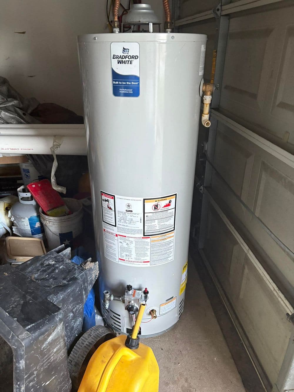 Bradford White water heater in garage, showing safety labeling and plumbing details.