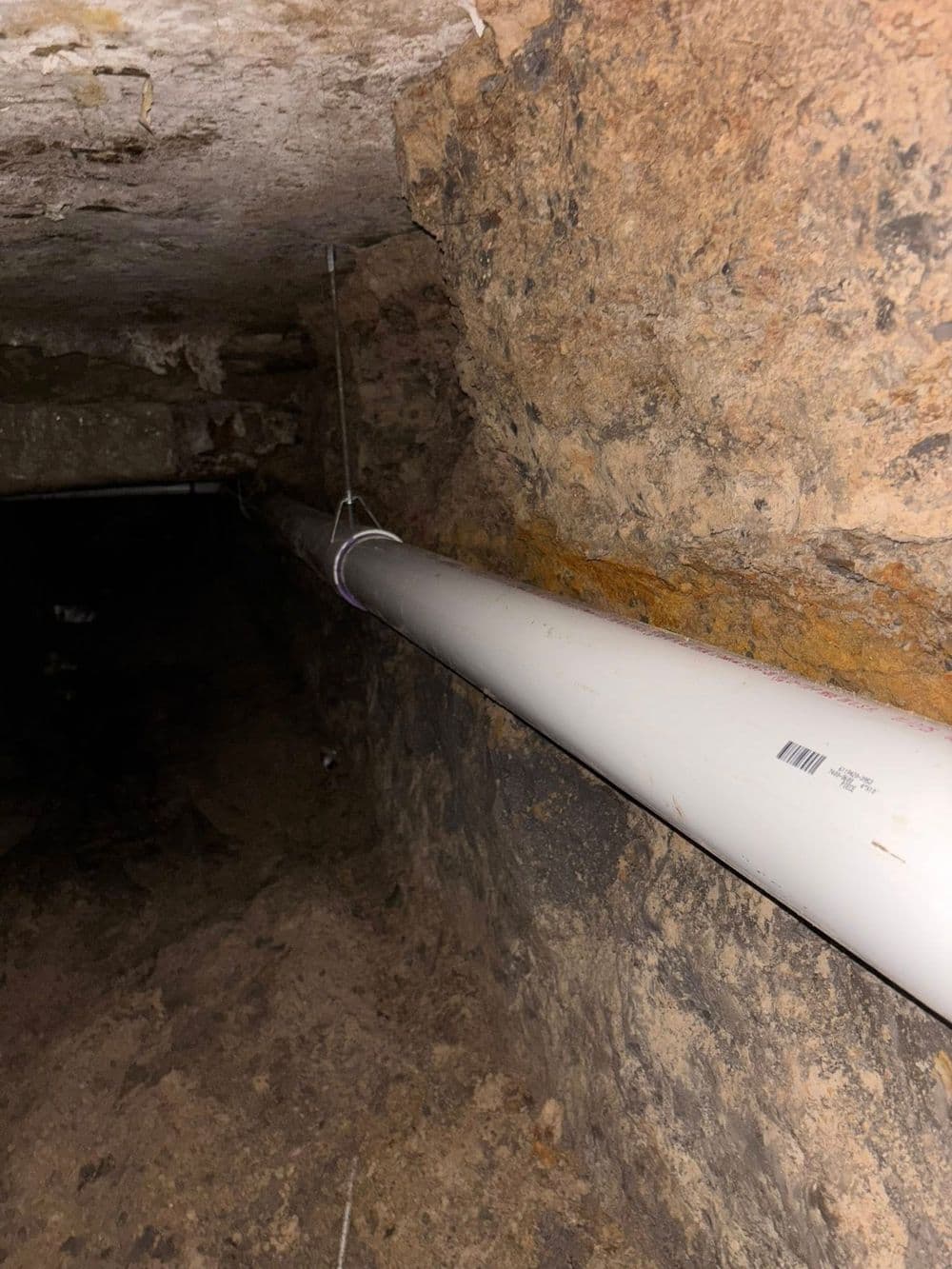 PVC pipe installed in a dark, rocky underground space with exposed earth.