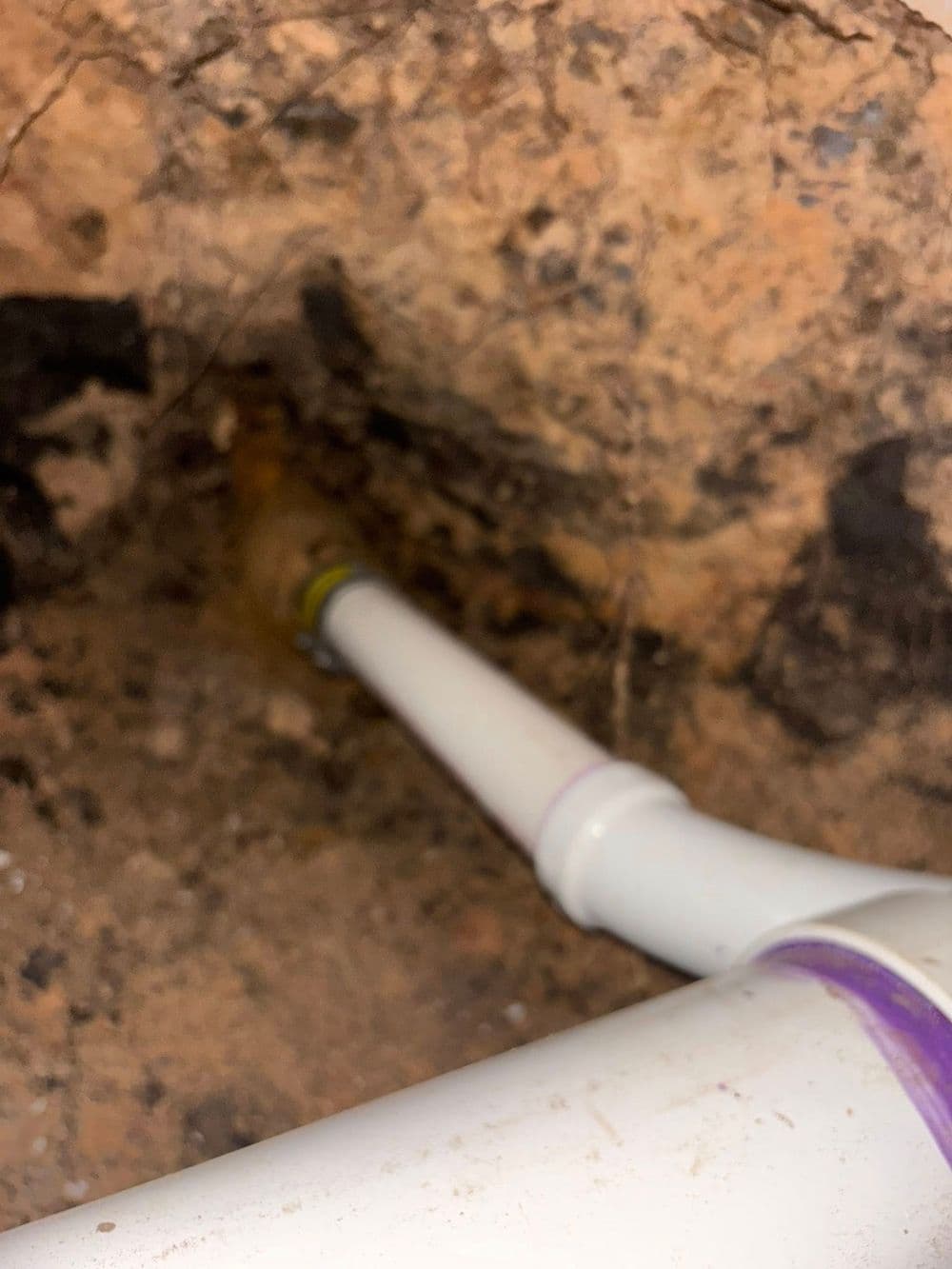 PVC plumbing pipe in a damp underground area with soil and debris.