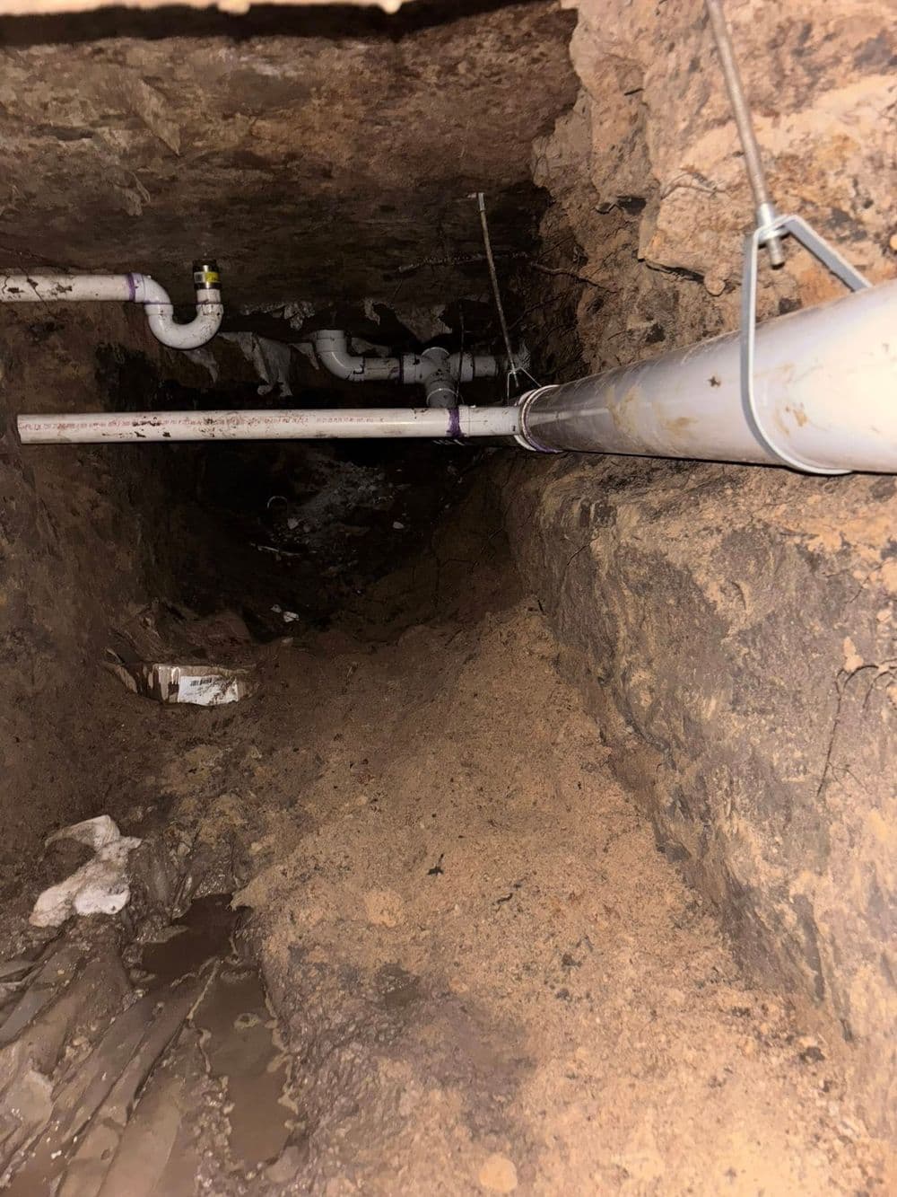 Underground view showing pipes and sandy soil in a dimly lit space.