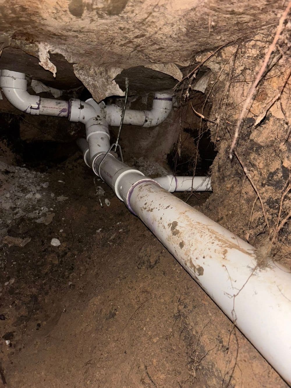 Underground PVC pipes installed beneath soil, showing dirt and roots around the pipes.