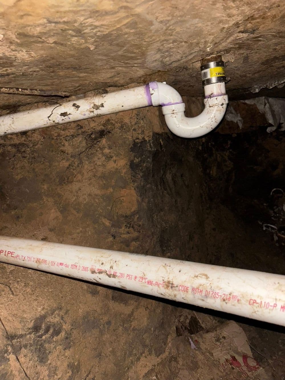 Underground plumbing installation with PVC pipes and fittings in a dirt setting.