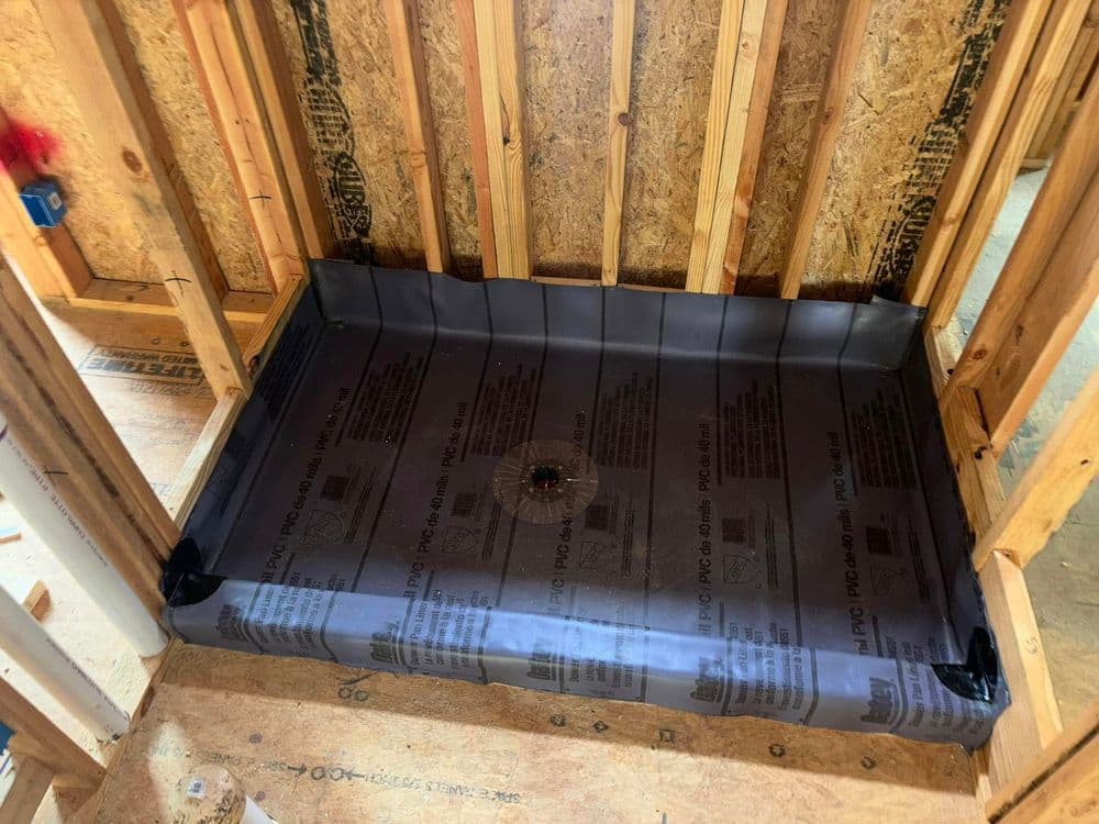 Waterproof shower pan installation in wooden framing, featuring protective barrier and drain assembly.