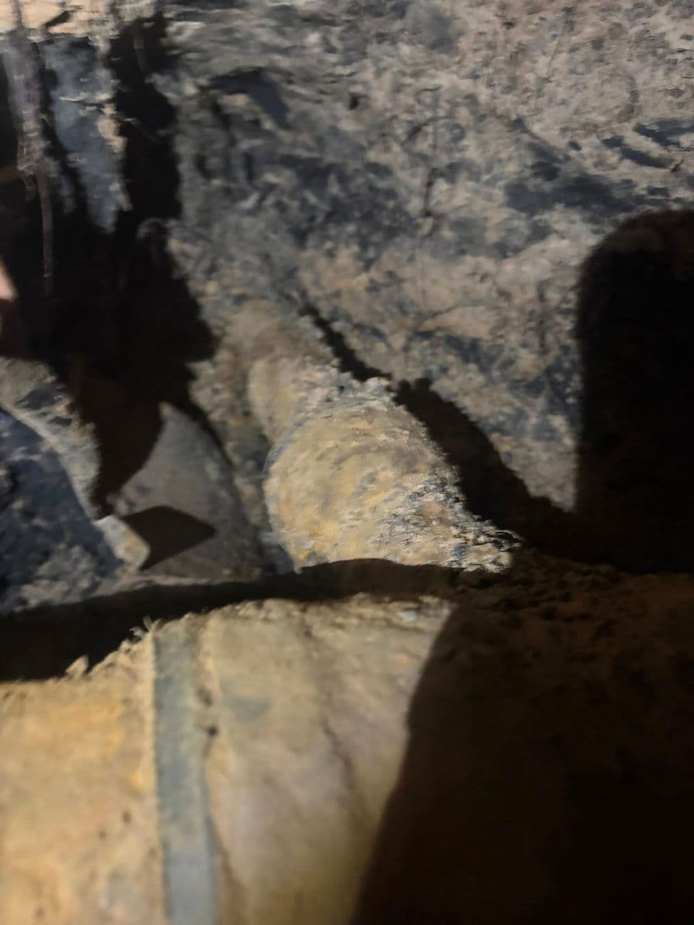 Corroded pipe in a damp underground setting, showing significant wear and dirt accumulation.