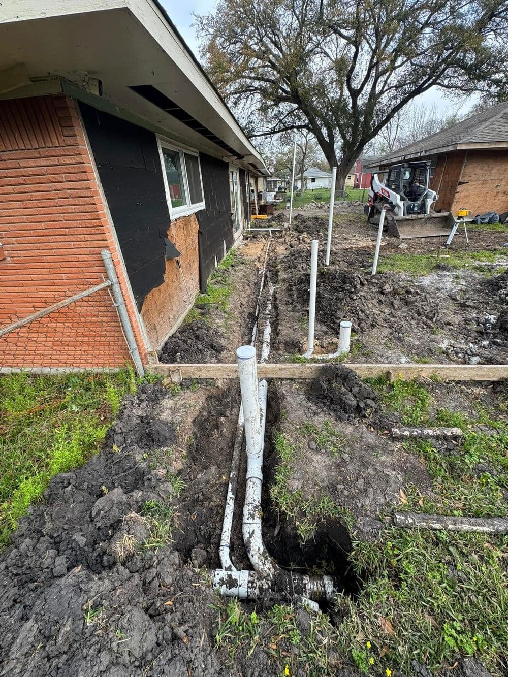 Newly installed PVC plumbing pipes along a residential foundation with excavation work visible.