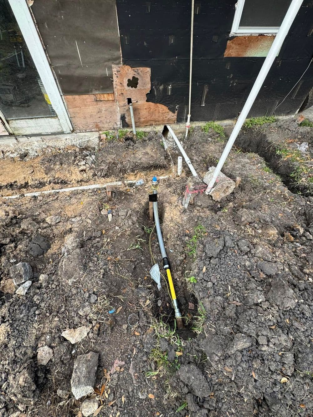 Construction site showing exposed plumbing lines and excavation near a building foundation.