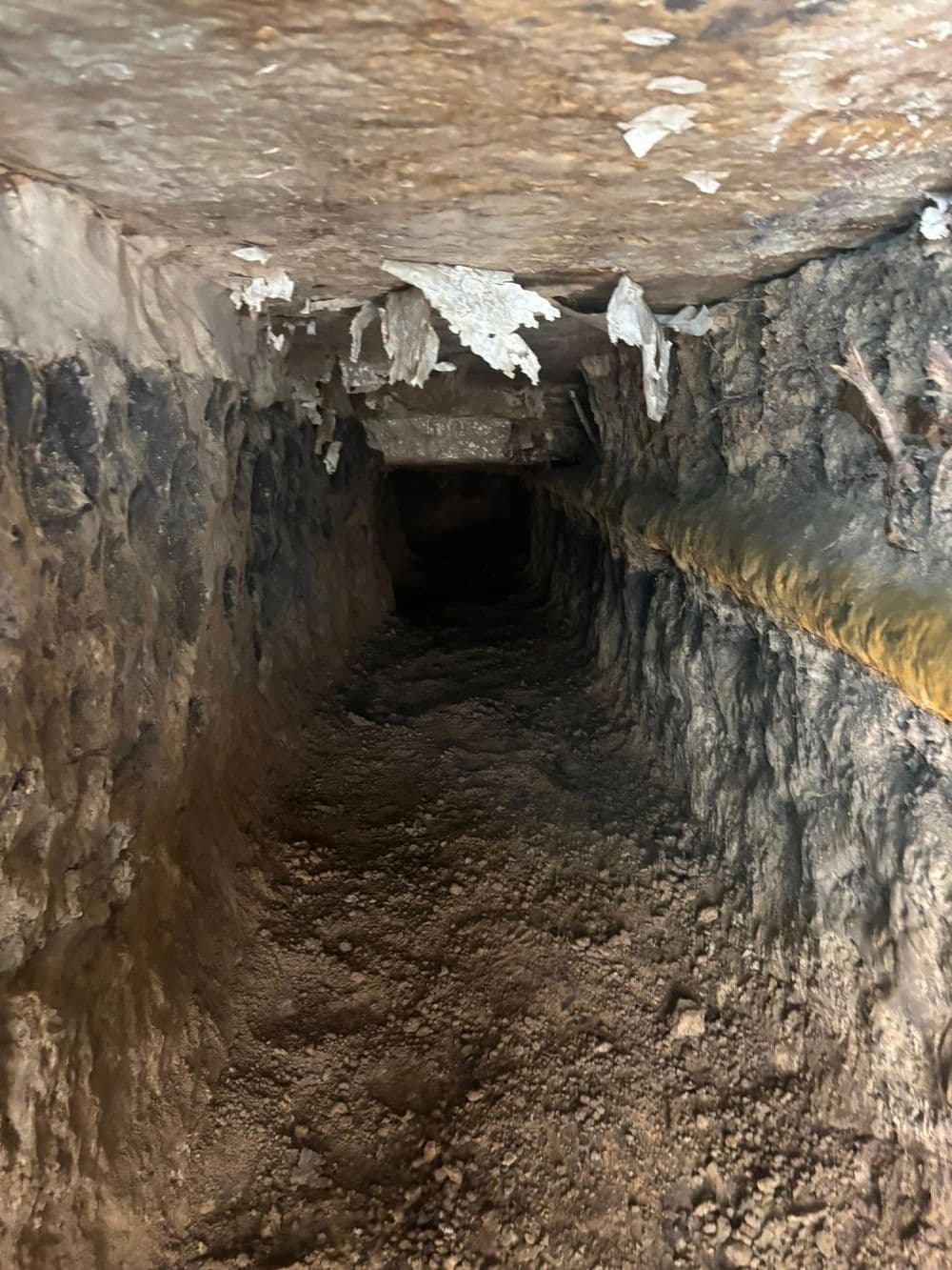 Dark subterranean tunnel with rough stone walls and debris on the ground.