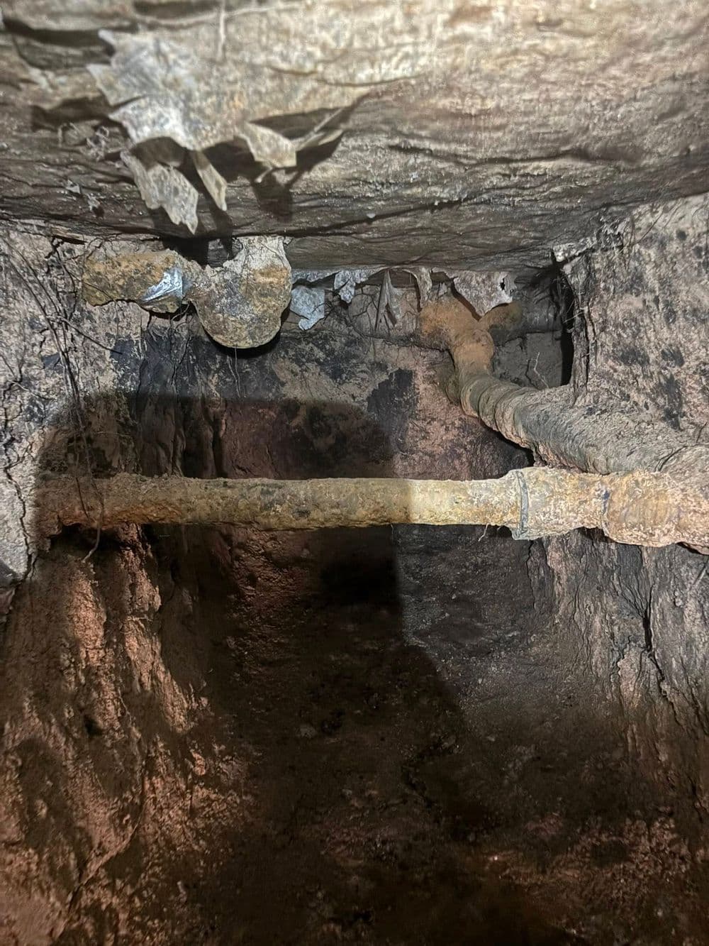 Exposed rusty pipes inside a dark, rocky underground area, showing signs of decay.